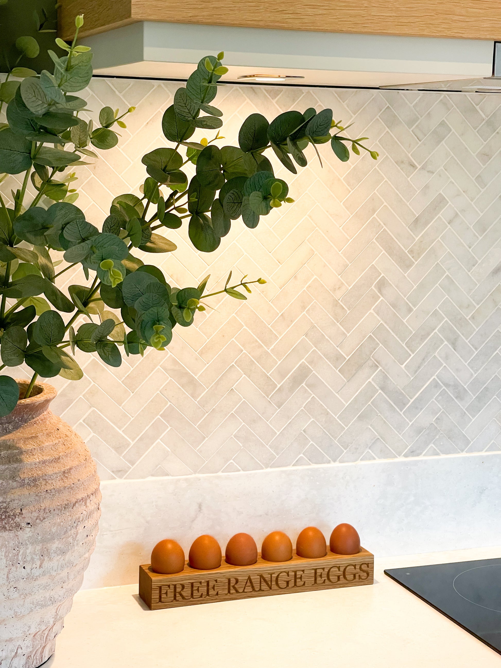 Egg storage holder on a white marble kitchen surface, with herringbone tiling in the background